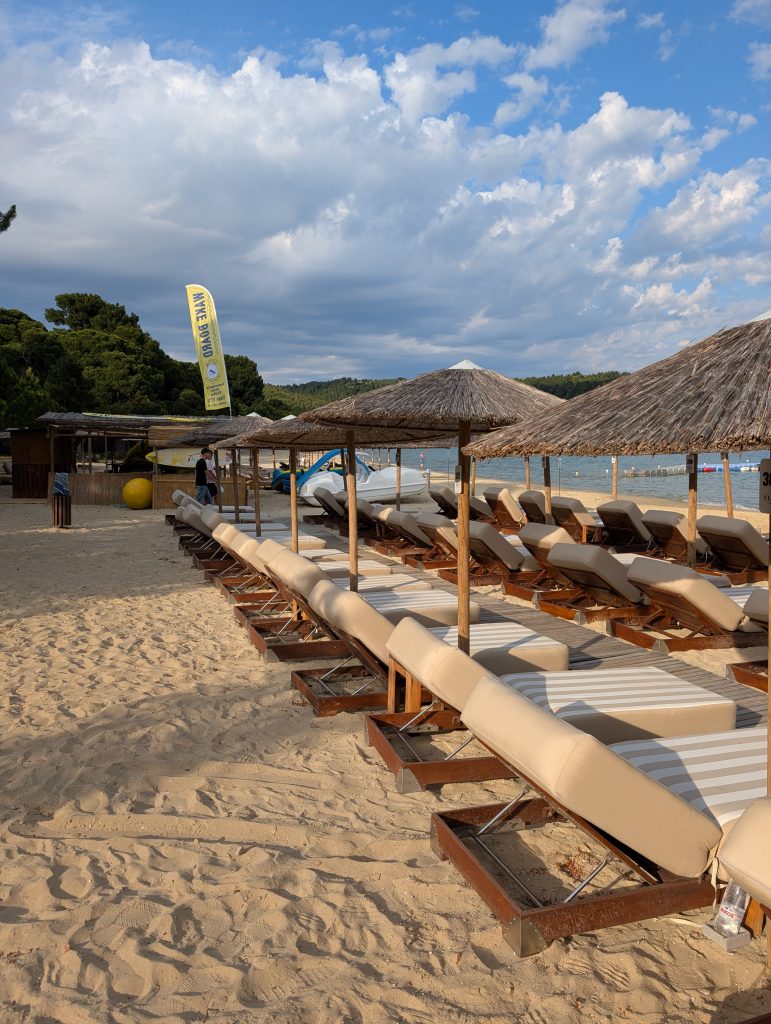 Luxurious sun loungers lined up on the golden sand of koukounaires with grass parasols dotted between them.