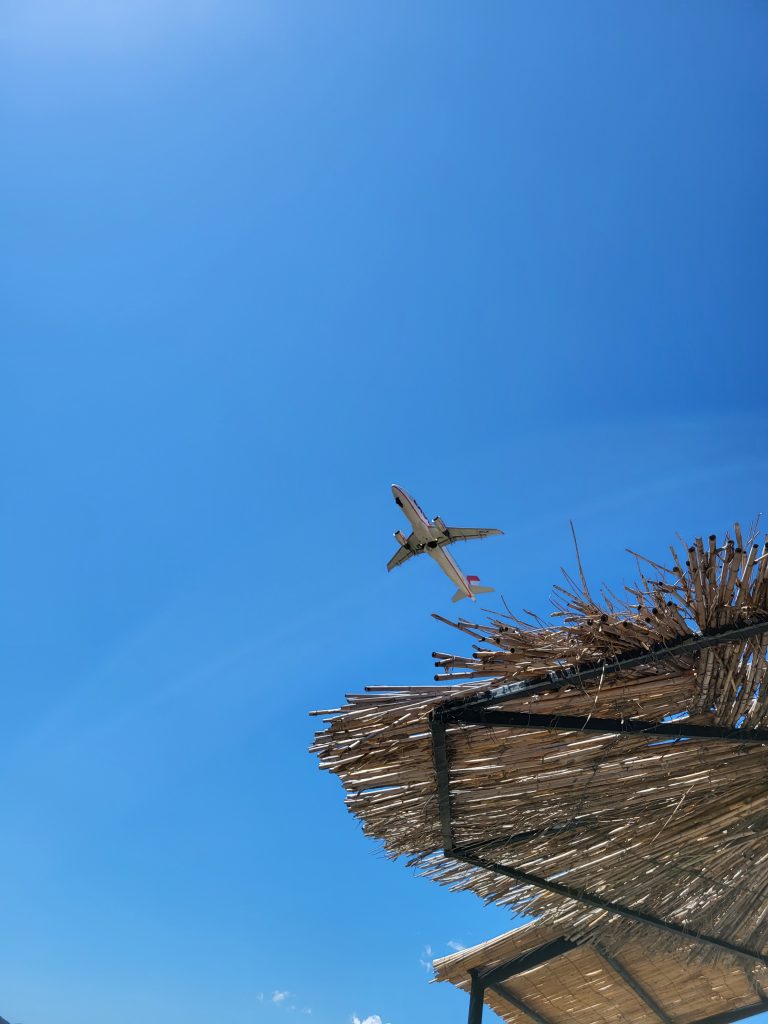 A plane flying over a grass parasol as it departs from Zante airport