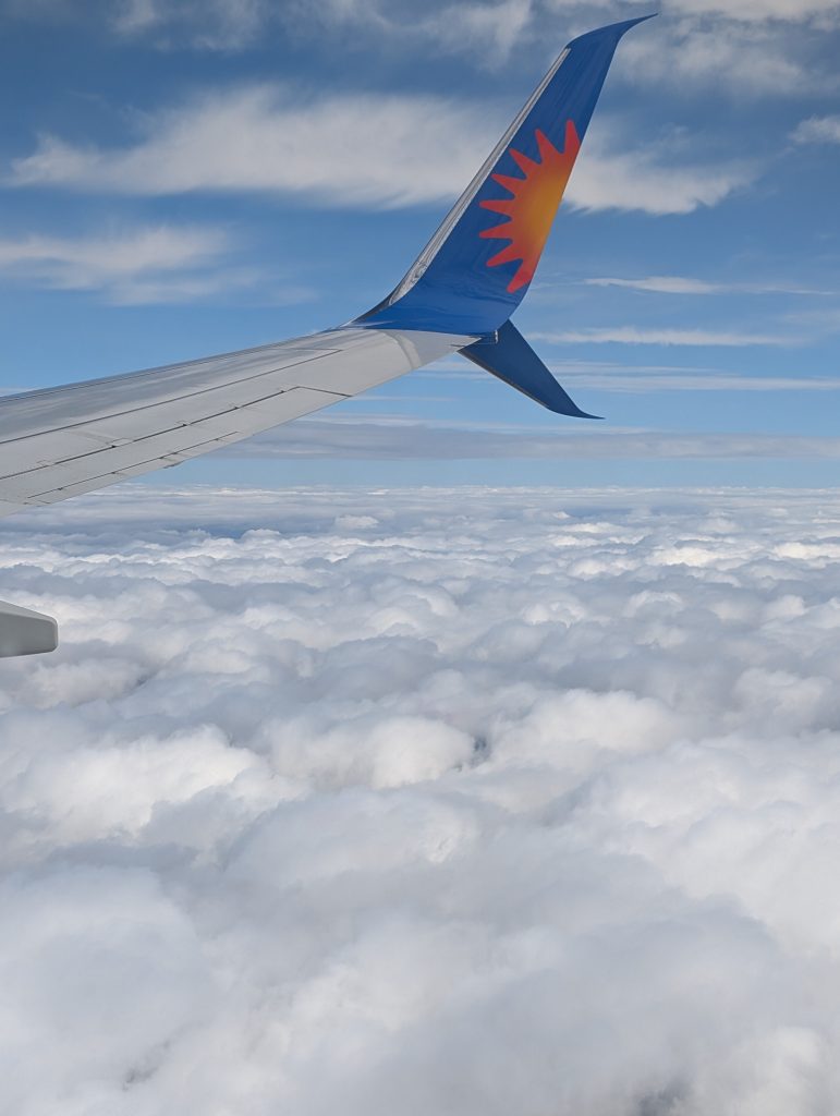 The wing of a plane with fluffy white clouds underneath