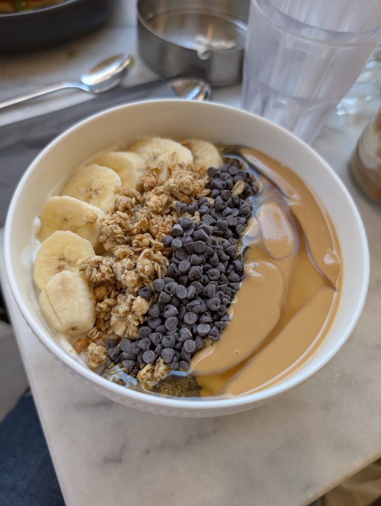 A yoghurt bowl with toppings of banana, granola, peanut butter and chocolate chips